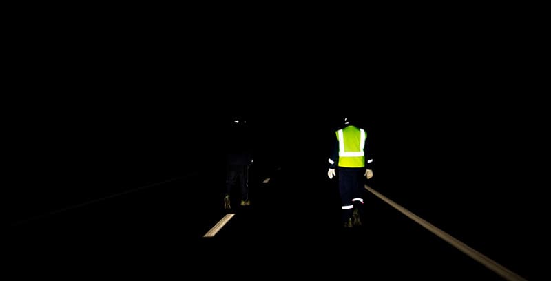 Comparativa de un trabajador con ropa oscura y otro con ropa de alta visibilidad en un entorno nocturno.