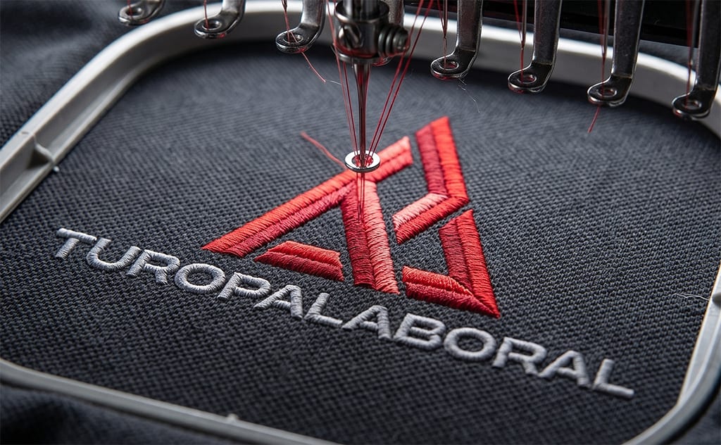 Máquina de bordado profesional personalizando ropa de trabajo con logo corporativo
